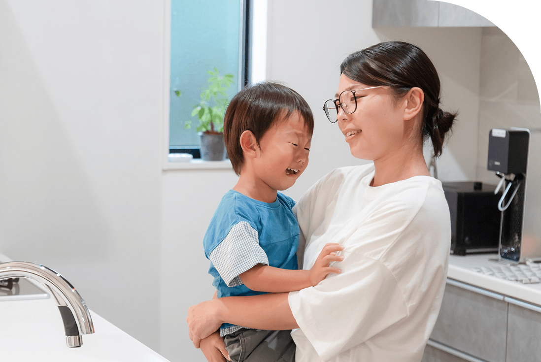 台所で泣いている男の子を抱き上げ、見つめる母親の様子。