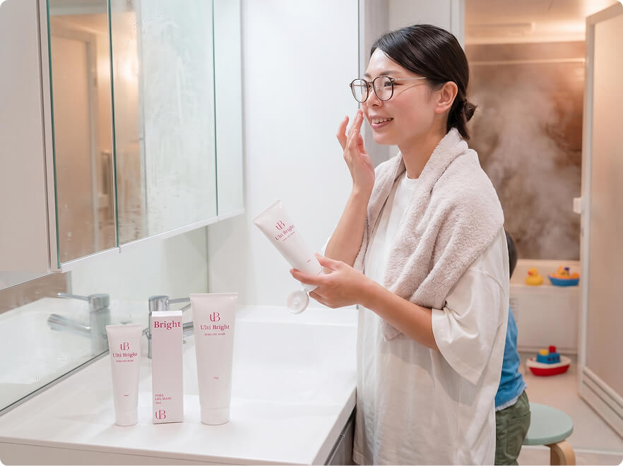 洗面台の前でタオルをかけ、チューブからクリームを頬に塗る笑顔の女性