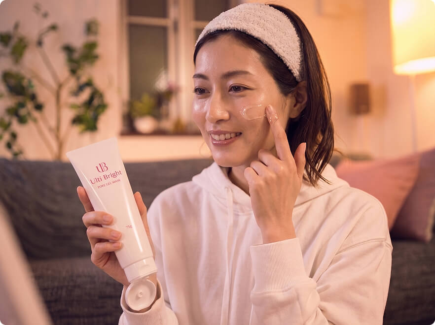 温かな間接証明の室内で、ヘアバンドをした女性がUlti Brightを持ち、頬にクリームを塗っている様子